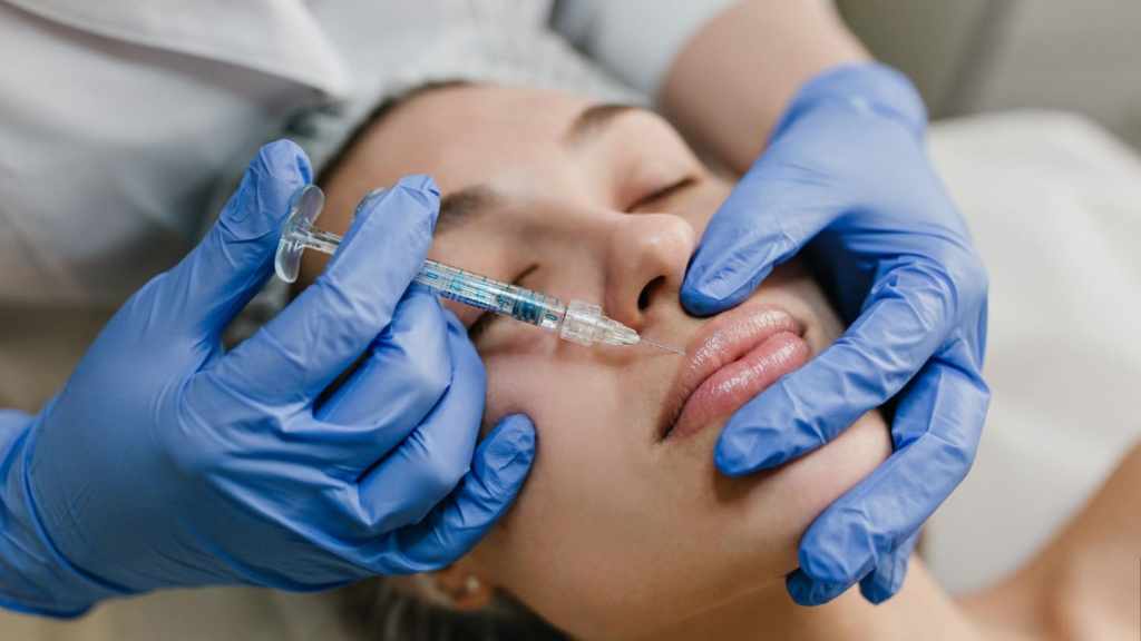 Close-up of a woman receiving a Botox lip flip injection by a medical professional wearing blue gloves, showing the cosmetic procedure in progress.