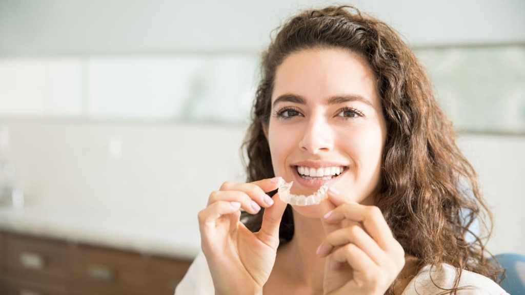 Woman holding a clear Invisalign aligner, illustrating how Invisalign can help correct an overbite.